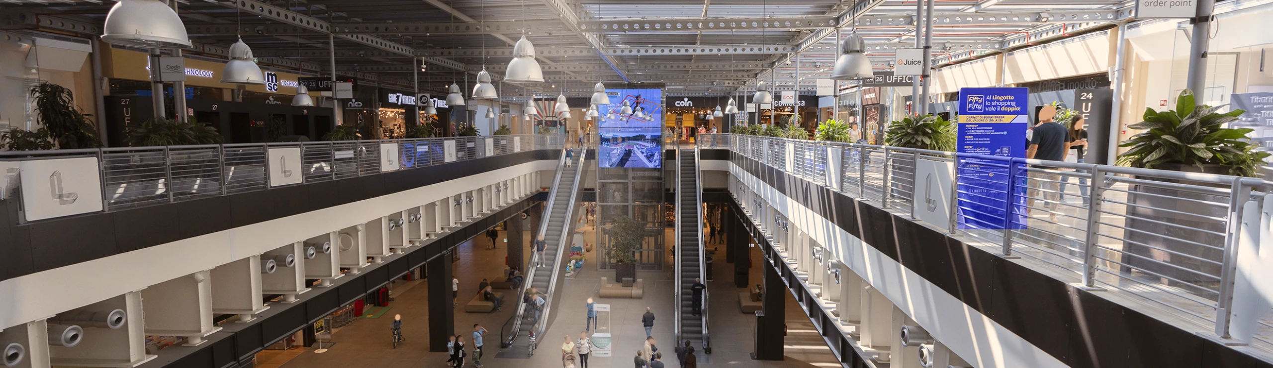 centro-commerciale-lingotto-nel-cuore-di-torino-home-page Atrio interno centro commerciale con scale mobili e schermo LED