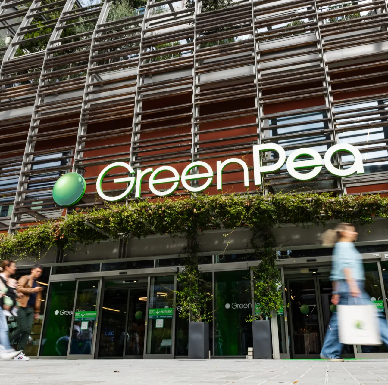 lingotto-GREEN-PEA Ingresso principale Green Pea Torino, insegna verde, facciata in legno e dettagli vegetali, persone in movimento