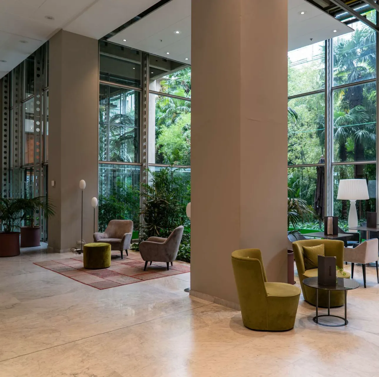 lingotto-hotel-2 Lobby moderna di hotel o lounge Lingotto Torino con poltrone colorate, pareti vetrate e vista sul giardino interno.