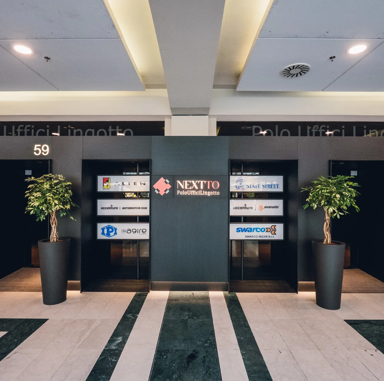 lingotto-next-to Ingresso Polo Uffici NEXTTO Lingotto Torino, piante ornamentali ai lati, segnaletica luminosa e loghi di aziende partner.
