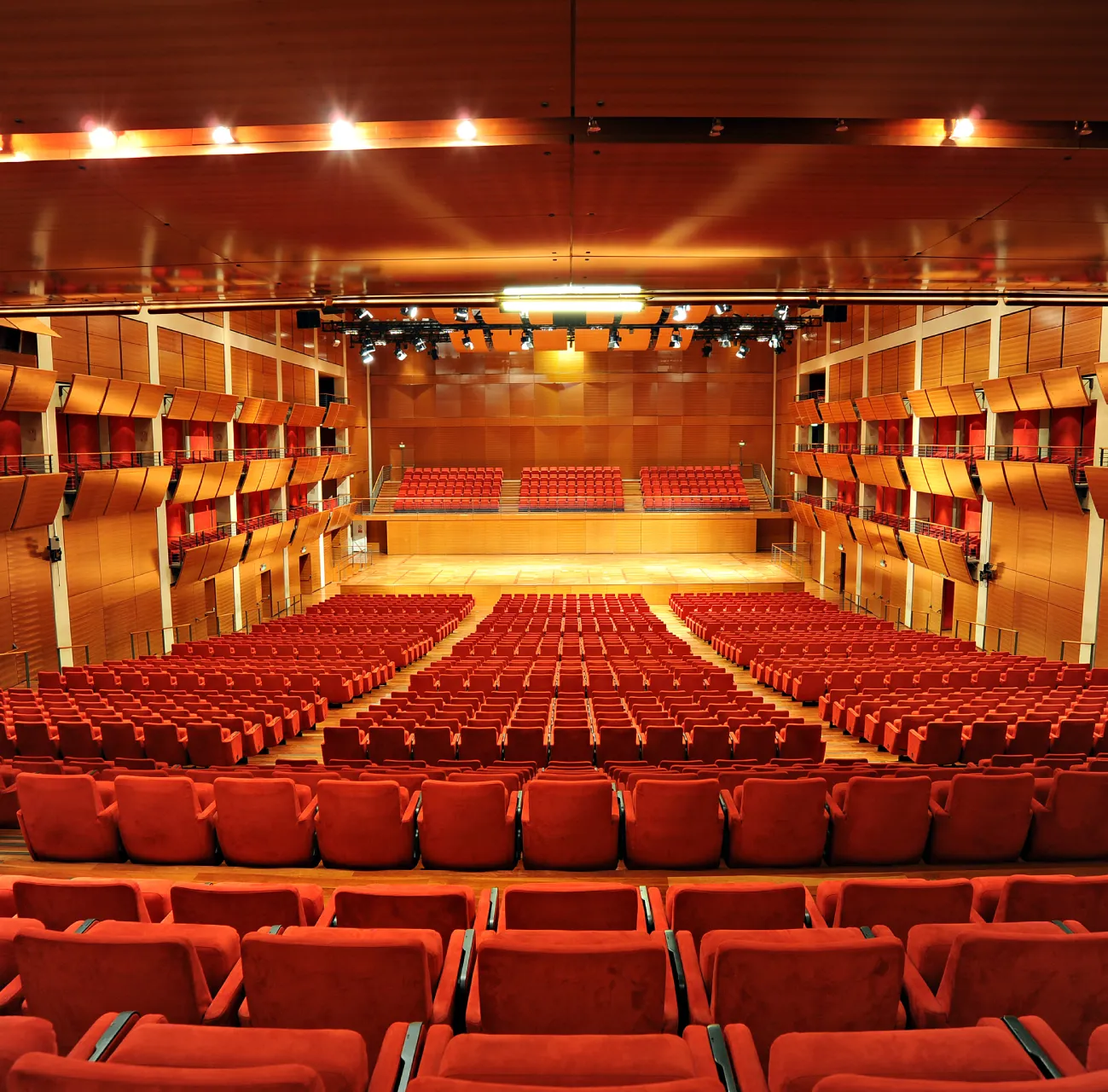 centro-commerciale-lingotto-centro-congressi Interno dell’Auditorium Lingotto Torino con centinaia di poltrone rosse, palco centrale e pareti in legno.