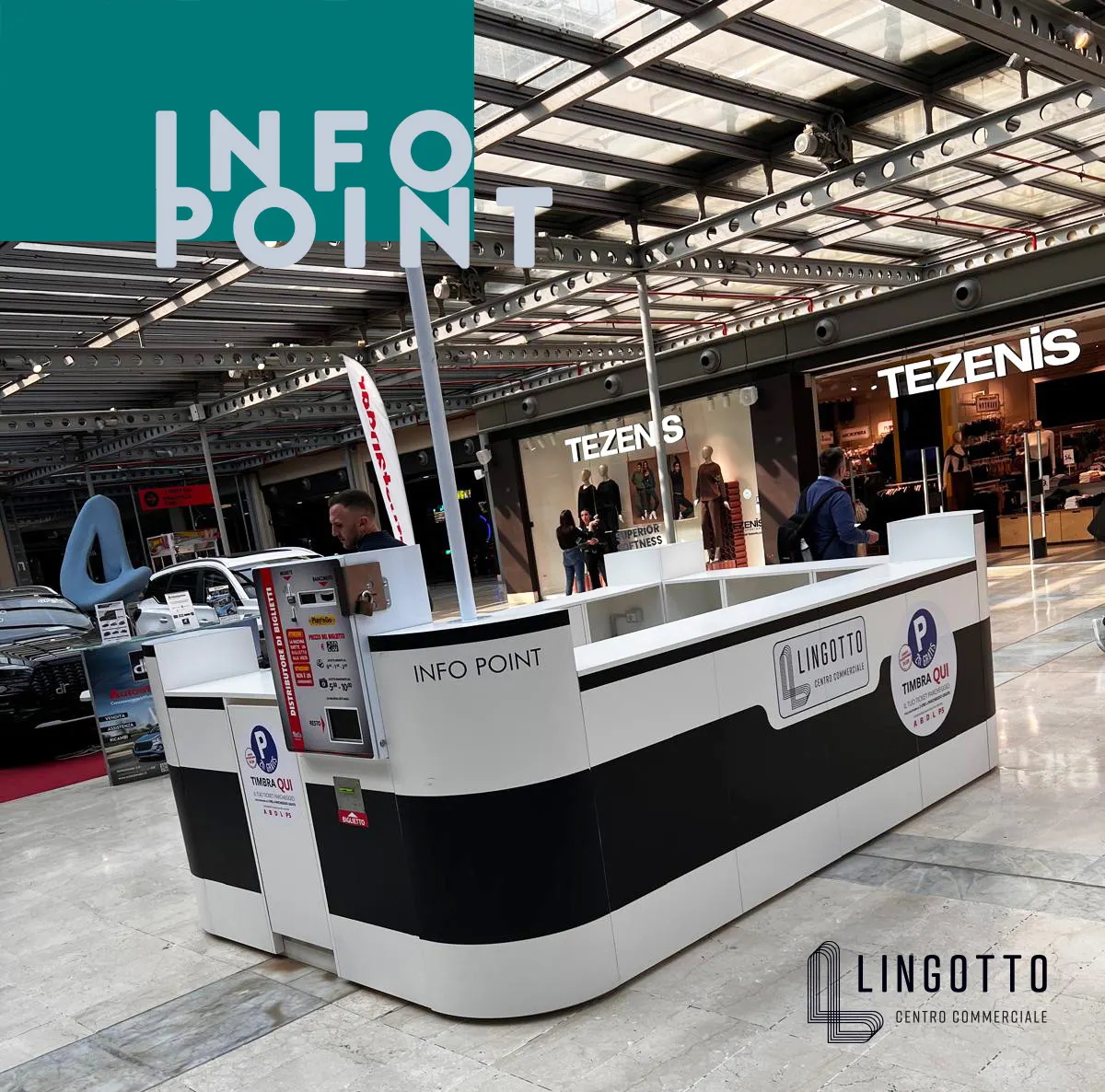 Info point del centro commerciale Lingotto con desk bianco e nero, personale e negozi Tezenis sullo sfondo.