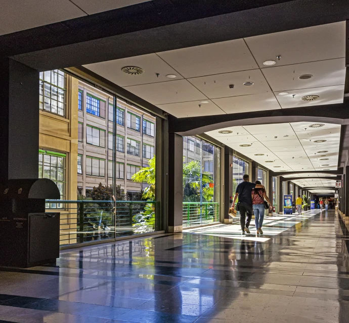 Galleria pedonale interna del Lingotto Torino con grandi vetrate, luce naturale, palme esterne e persone che passeggiano.