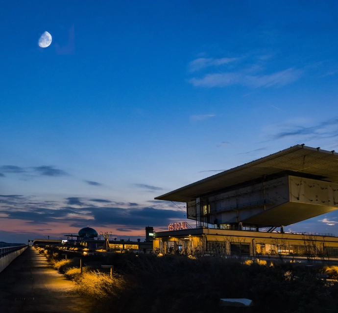 Vista serale Lingotto Torino con luna, tetto panoramico illuminato e installazione luminosa “YES TO ALL”.