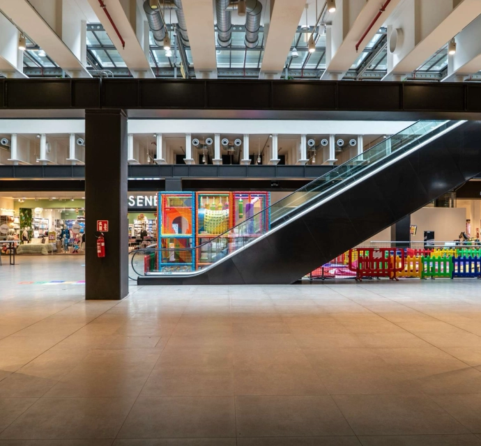 Interno moderno Lingotto Torino con scala mobile, area giochi recintata per bambini e negozi sullo sfondo.