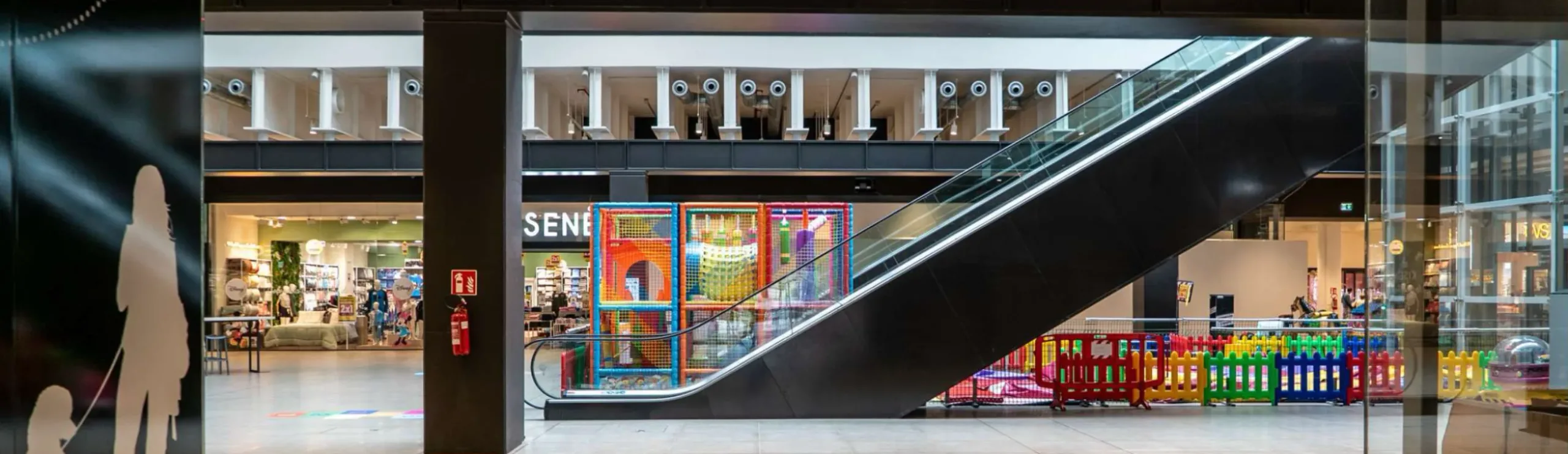 Interno centro commerciale Lingotto Torino, scala mobile, area giochi recintata per bambini e negozi sullo sfondo