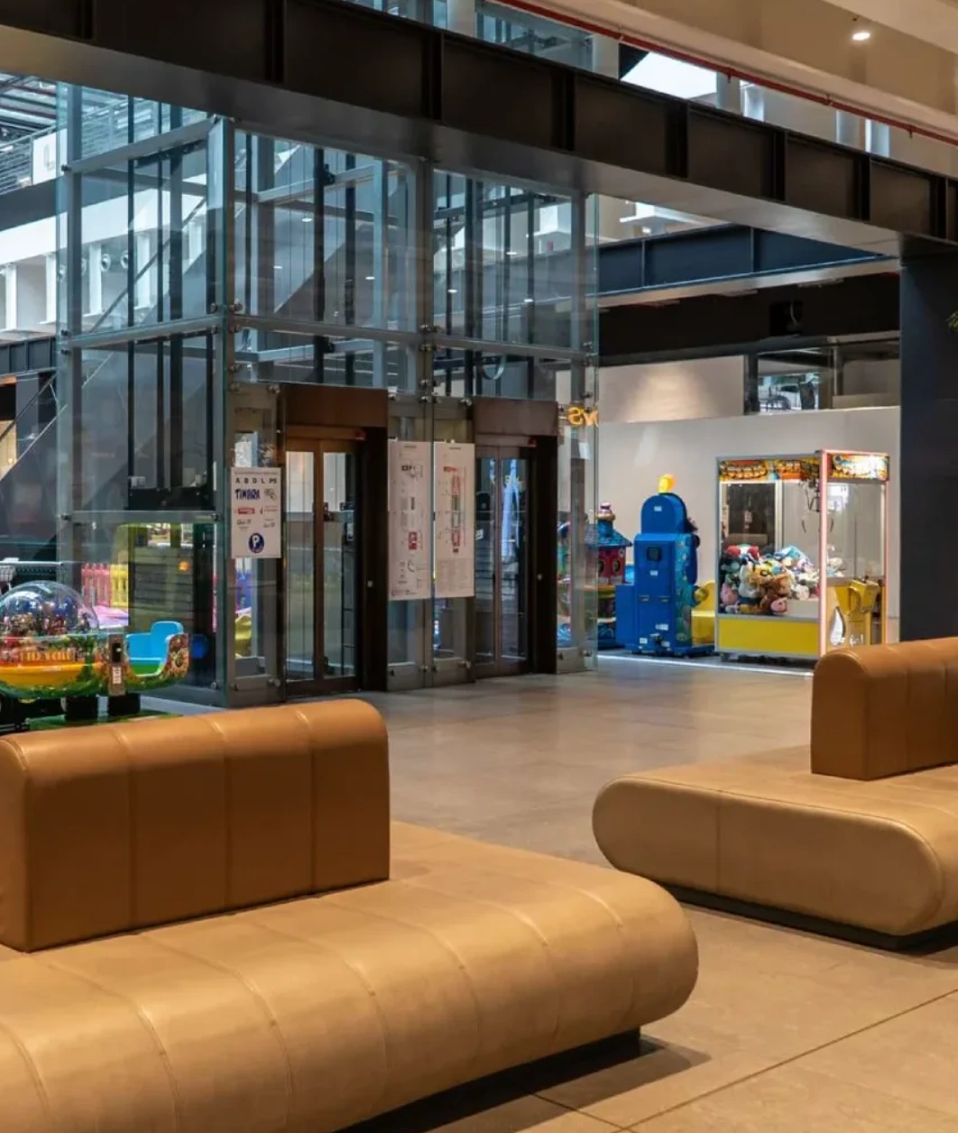 Atrio interno del Lingotto Torino con ascensore panoramico in vetro, divanetti beige e area giochi per bambini.